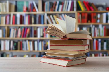 Tahta bir masanın üzerinde yığılı kitaplar..