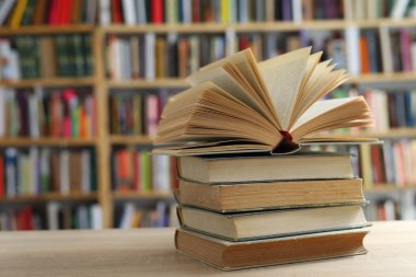 Kütüphanenin arka planına karşı ahşap bir masanın üzerindeki kitap yığını