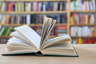 Açık bir kitap, ahşap masa üzerinde kitaplar.