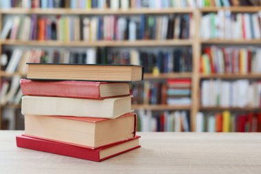 Okul kütüphanesindeki ahşap rafta yığınla kitap var.