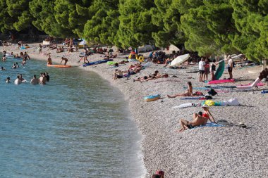 Makarska, Hırvatistan, 30.07.2025. Hırvatistan 'da yıllık tatil yapan turistler deniz ve güneşin keyfini çıkarırken, deniz sahilinde şişme yüzüklü bir kadın mayo giyiyor. yüksek kaliteli fotoğraf