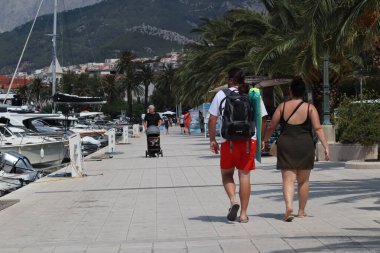 Makarska, Hırvatistan, 12.08.2025. Hırvatistan 'da yıllık tatil yapan turistler, yat ile marina caddesinde yürüyen erkek ve kadın, deniz ve güneşin keyfini çıkarıyorlar..