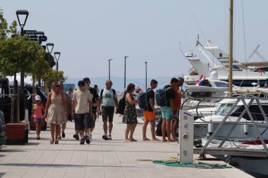 Makarska, Hırvatistan, 12.08.2025. Hırvatistan 'da yıllık tatil yapan turistler, yat ile marina caddesinde yürüyen erkek ve kadın, deniz ve güneşin keyfini çıkarıyorlar..