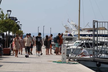 Makarska, Hırvatistan, 12.08.2025. Hırvatistan 'da yıllık tatil yapan turistler, yat ile marina caddesinde yürüyen erkek ve kadın, deniz ve güneşin keyfini çıkarıyorlar..