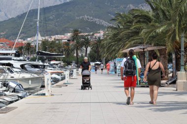 Makarska, Hırvatistan, 12.08.2025. Hırvatistan 'da yıllık tatil yapan turistler, yat ile marina caddesinde yürüyen erkek ve kadın, deniz ve güneşin keyfini çıkarıyorlar..