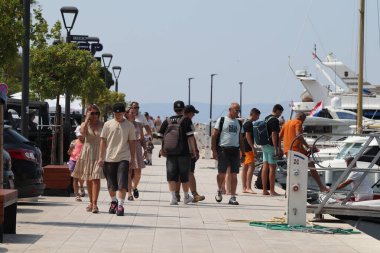 Makarska, Hırvatistan, 12.08.2025. Hırvatistan 'da yıllık tatil yapan turistler, yat ile marina caddesinde yürüyen erkek ve kadın, deniz ve güneşin keyfini çıkarıyorlar..