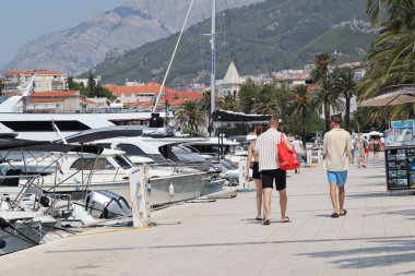 Makarska, Hırvatistan, 12.08.2025. Hırvatistan 'da yıllık tatil yapan turistler, yat ile marina caddesinde yürüyen erkek ve kadın, deniz ve güneşin keyfini çıkarıyorlar..