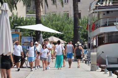 Makarska, Hırvatistan, 12.08.2025. Hırvatistan 'da yıllık tatil yapan turistler, yat ile marina caddesinde yürüyen erkek ve kadın, deniz ve güneşin keyfini çıkarıyorlar..