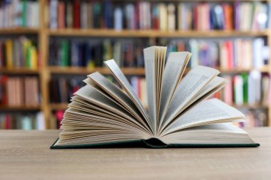 Kütüphanede yığınla kitap. Arkaplanda kitaplarla dolu bir masanın üzerinde açık bir kitap. Bilgi ve keşfe adanmış bir an.