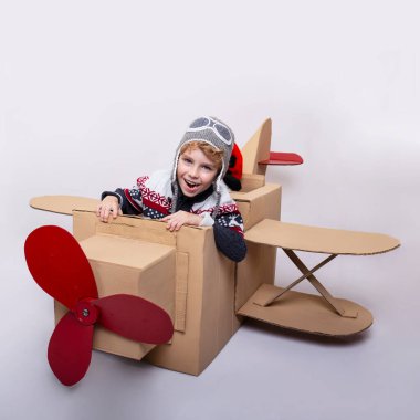 Beyaz arka planda pilotluk yaptığını hayal ederken karton uçakta oturan küçük bir çocuğun ön görüntüsü..
