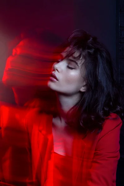 Profile image of young woman with makeup and hairstyle, wear red suit, with closed eyes, red neon studio light.