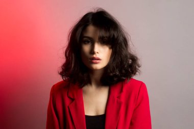 Makyajlı ve saç stili olan güzel bir kadının moda imajı, kırmızı takım elbise, kırmızı neon ışıklı stüdyo..