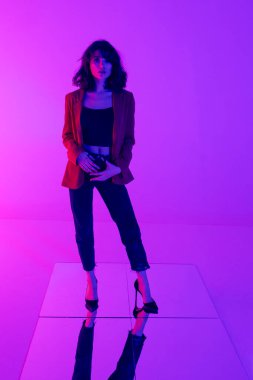 Kırmızı elbiseli çekici esmer bir mankenin tam boy fotoğrafı. Neon ışıklı siyah kot..