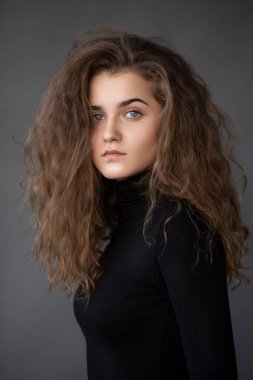 Front image portrait of a girl with curly hair, dressed in a black , on a grey background.