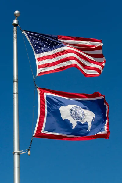 Wyoming state flag and the American flag waving in a blue sky, vertical