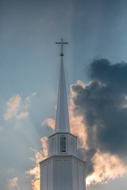 Çapraz ve kilise çan kulesi, güneş ışığı ve arka planda mavi gökyüzü, dikey.