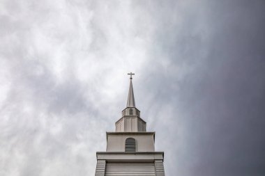 Tepesinde haç olan kilise kulesi dramatik, bulutlu, yatay gökyüzüne karşı yükselir.