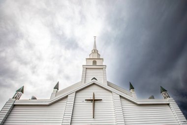 Tepesinde haç olan kilise kulesi dramatik, bulutlu, yatay gökyüzüne karşı yükselir.