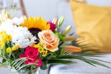 Çiçeklerle dolu bir salonda. Arka tarafta bir kanepe var.