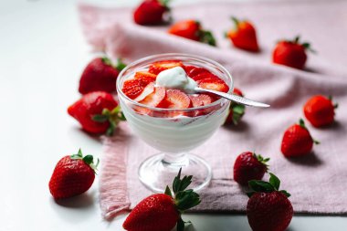 Zengin Yunan yoğurdunun üzerinde taze dilimlenmiş çilek ve bir kaşık dolusu yemeğin tadını çıkarmak üzere. Temiz, minimalist yemek fotoğrafçılığı.
