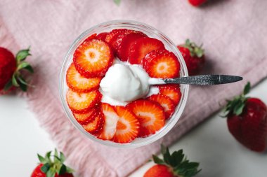 Bir kaşık kremalı Yunan yoğurdu ve çileği kaldıran bir elin yakın çekimi. Temiz bir arkaplanda taze ve besleyici bir gıda konsepti.