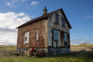 Çiftliği olan terk edilmiş eski bir ev. İzlanda deniz kıyısına yakın bir alan. Açık çimenler. Beyaz bulutlu mavi gökyüzü. Holmsvollur, Sudurnesjabaer, İzlanda.