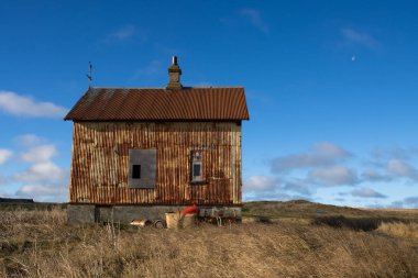 Çiftliği olan terk edilmiş eski bir ev. İzlanda deniz kıyısına yakın bir alan. Açık çimenler. Beyaz bulutlu mavi gökyüzü. Holmsvollur, Sudurnesjabaer, İzlanda.