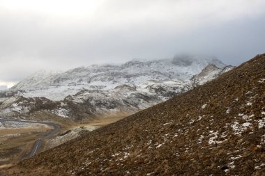 Sonbaharda ilk kar yağan dağların arasında ve çevresinde yüksek kaliteli yollar. Zemin liken ile kaplıydı. Bulutlu gökyüzü. Adanın güneybatı kesimi, Nesjavallavegur (Nesjavellir), İzlanda.