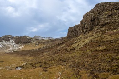Adanın orta batısındaki dağlar. Zemin liken ve sonbaharda taze kar ile kaplıydı. Dramatik bulutlu gökyüzü. Onefnedur Vegur, İzlanda.