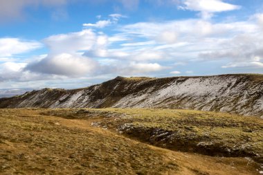Zemin yosunlarla kaplı, dağların yüksek kesimlerinde ilk sonbahar karı var. Beyaz bulutlu mavi gökyüzü. Onefndur vegur, İzlanda.