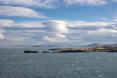 Calm water of the famous big lake Thingvallavatn. Mountains covered by snow in the background. Blue sky with white clouds. Onefndur vegur, Iceland.