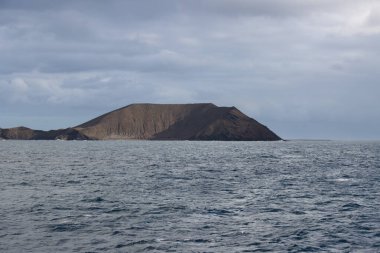 Calm dark water of the Atlantic ocean. Isla los Lobos on the horizon. Intenese clouds on the sky. Isla los Lobos, Canary Islands, Spain.