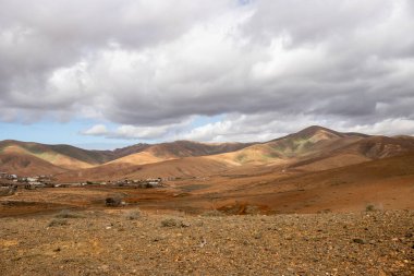 Light brown tone of the soil. Waves of the volcanic mountains in the background. Intense clouds in the winter. Municipio (municipality) de Pajara, Fuerteventura, Canary Islands, Spain.