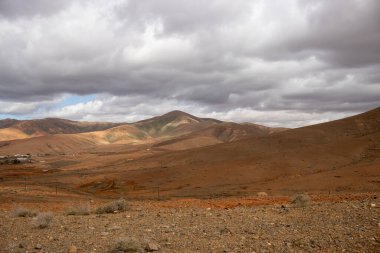 Light brown tone of the soil. Waves of the volcanic mountains in the background. Intense clouds in the winter. Municipio (municipality) de Pajara, Fuerteventura, Canary Islands, Spain.