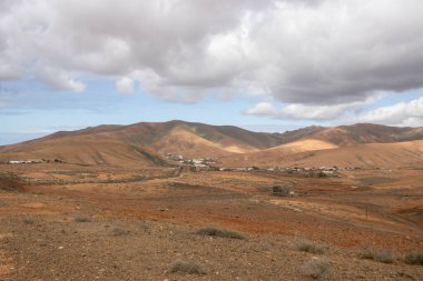 Light brown tone of the soil. Waves of the volcanic mountains in the background. Intense clouds in the winter. Municipio (municipality) de Pajara, Fuerteventura, Canary Islands, Spain.