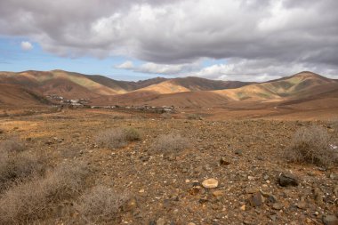 Light brown tone of the soil. Waves of the volcanic mountains in the background. Intense clouds in the winter. Municipio (municipality) de Pajara, Fuerteventura, Canary Islands, Spain.