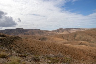 Shapes and lines of the mountains of the volcanic origin. Light brown color of the soil. Sky with clouds in the winter. Mirador Astronomico (Astronimical Viewpoint), Fuerteventura, Canary Islands