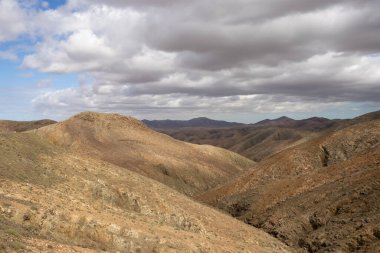 Shapes and lines of the mountains of the volcanic origin. Light brown color of the soil. Sky with clouds in the winter. Mirador Astronomico (Astronimical Viewpoint), Fuerteventura, Canary Islands