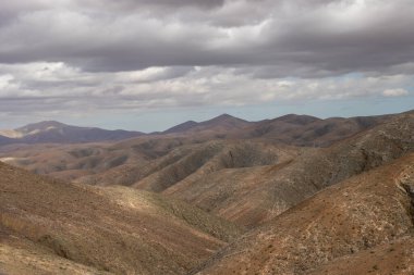 Shapes and lines of the mountains of the volcanic origin. Light brown color of the soil. Sky with clouds in the winter. Mirador Astronomico (Astronimical Viewpoint), Fuerteventura, Canary Islands