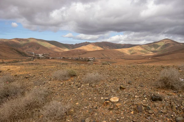 Light brown tone of the soil. Waves of the volcanic mountains in the background. Intense clouds in the winter. Municipio (municipality) de Pajara, Fuerteventura, Canary Islands, Spain.