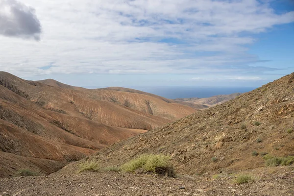 Shapes and lines of the mountains of the volcanic origin. Light brown color of the soil. Sky with clouds in the winter. Mirador Astronomico (Astronimical Viewpoint), Fuerteventura, Canary Islands