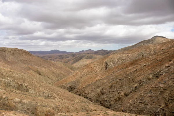 Shapes and lines of the mountains of the volcanic origin. Light brown color of the soil. Sky with clouds in the winter. Mirador Astronomico (Astronimical Viewpoint), Fuerteventura, Canary Islands