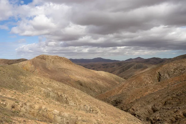 Shapes and lines of the mountains of the volcanic origin. Light brown color of the soil. Sky with clouds in the winter. Mirador Astronomico (Astronimical Viewpoint), Fuerteventura, Canary Islands