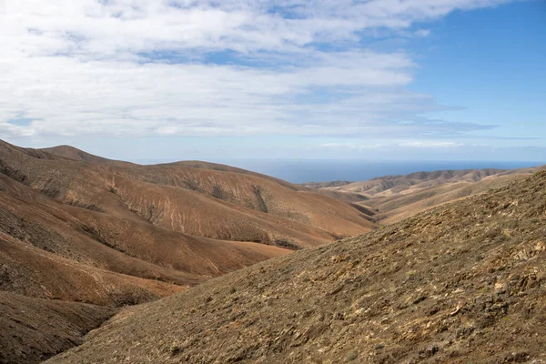 Shapes and lines of the mountains of the volcanic origin. Light brown color of the soil. Sky with clouds in the winter. Mirador Astronomico (Astronimical Viewpoint), Fuerteventura, Canary Islands