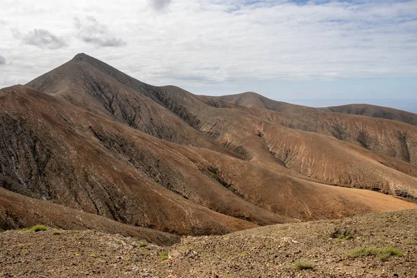 Shapes and lines of the mountains of the volcanic origin. Light brown color of the soil. Sky with clouds in the winter. Mirador Astronomico (Astronimical Viewpoint), Fuerteventura, Canary Islands