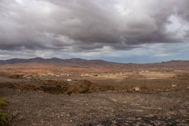 Light brown tone of the soil. Waves of the volcanic mountains in the background. Intense clouds in the winter. Almacigo, Fuerteventura, Canary Islands, Spain.