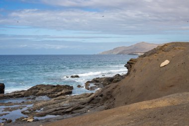 Coast of the Atlantic ocean with small waves. Sky with clouds in the winter. Various rock and stones on the coastline. Playa de la Pared, Fuerteventura, Canary Islands, Spain