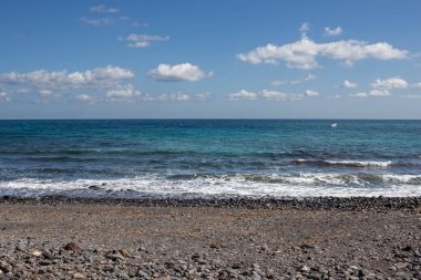 Kışın güneşli bir gün. Atlantik Okyanusu kıyısında küçük dalgalar. Çakıl taşlı plaj. Beyaz bulutlu mavi gökyüzü. Playa del Jablito, Fuerteventura, İspanya.