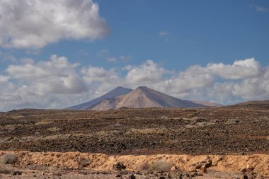 Taş volkanik çöl ve ufuktaki dağlar. Durch Park (Parque Holandes). Beyaz bulutlu mavi gökyüzü. Fuerteventura, UNESCO Biyosfer Rezervi 'dir. Kanarya Adaları, İspanya.