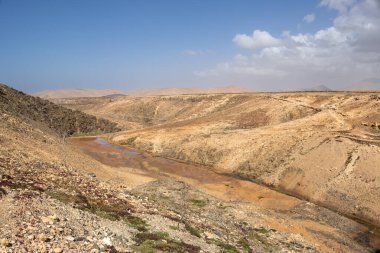 Bir vadide yer alan tatlı su deposunun kuru kısmı. Rocky Hills çevresi. Kışın beyaz bulutlu mavi gökyüzü. Molinos Mumyalaması, Fuerteventura, Kanarya Adaları, İspanya.
